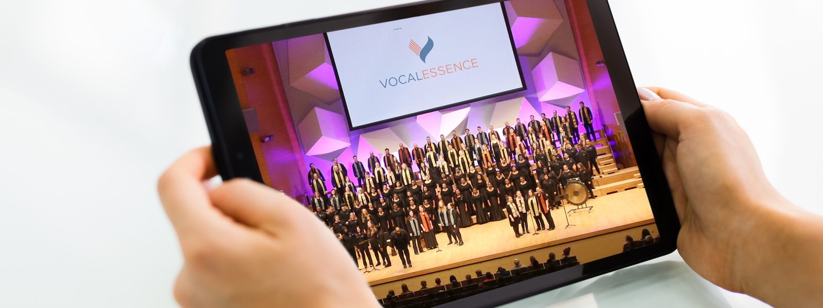 Hands holding tablet with image of many singers performing on stage