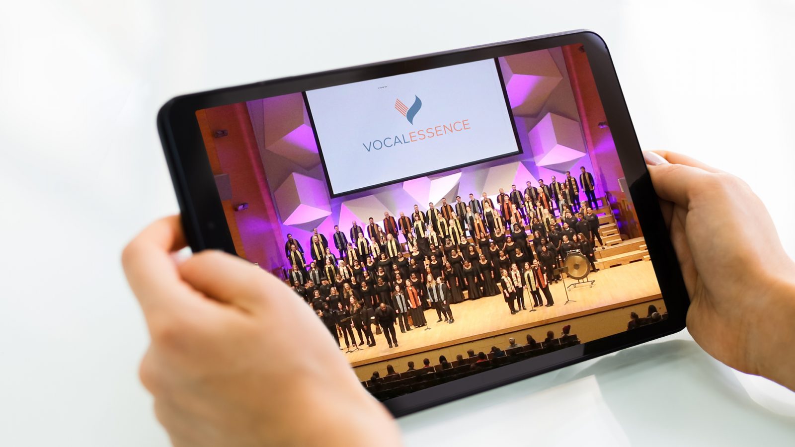 Hands holding tablet with image of many singers performing on stage
