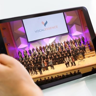 Hands holding tablet with image of many singers performing on stage