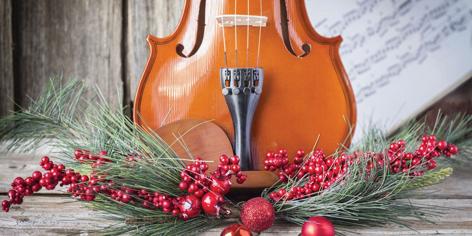 Violin in front of sheet music with pine, red berries, and red ornaments