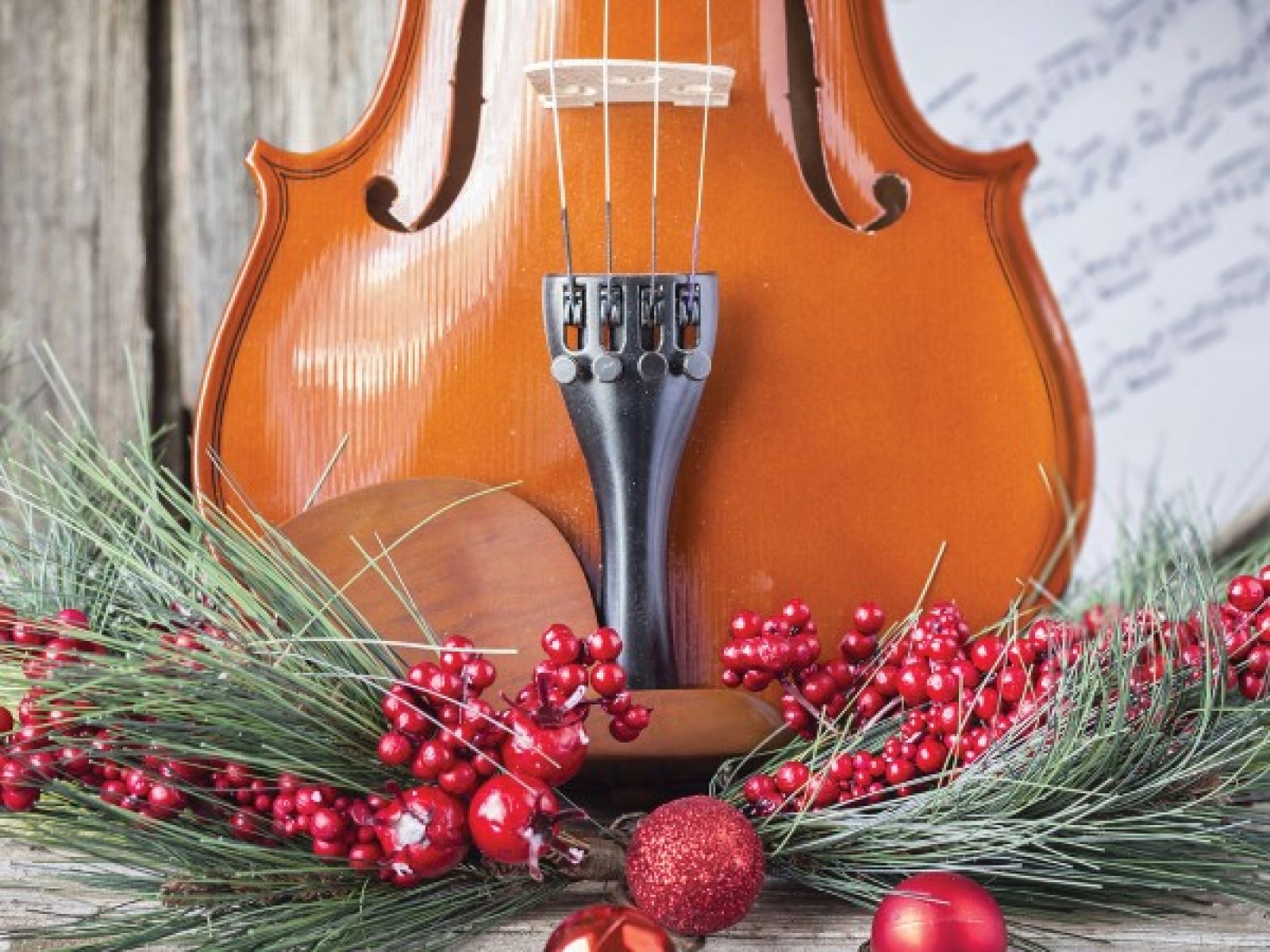 Violin in front of sheet music with pine, red berries, and red ornaments