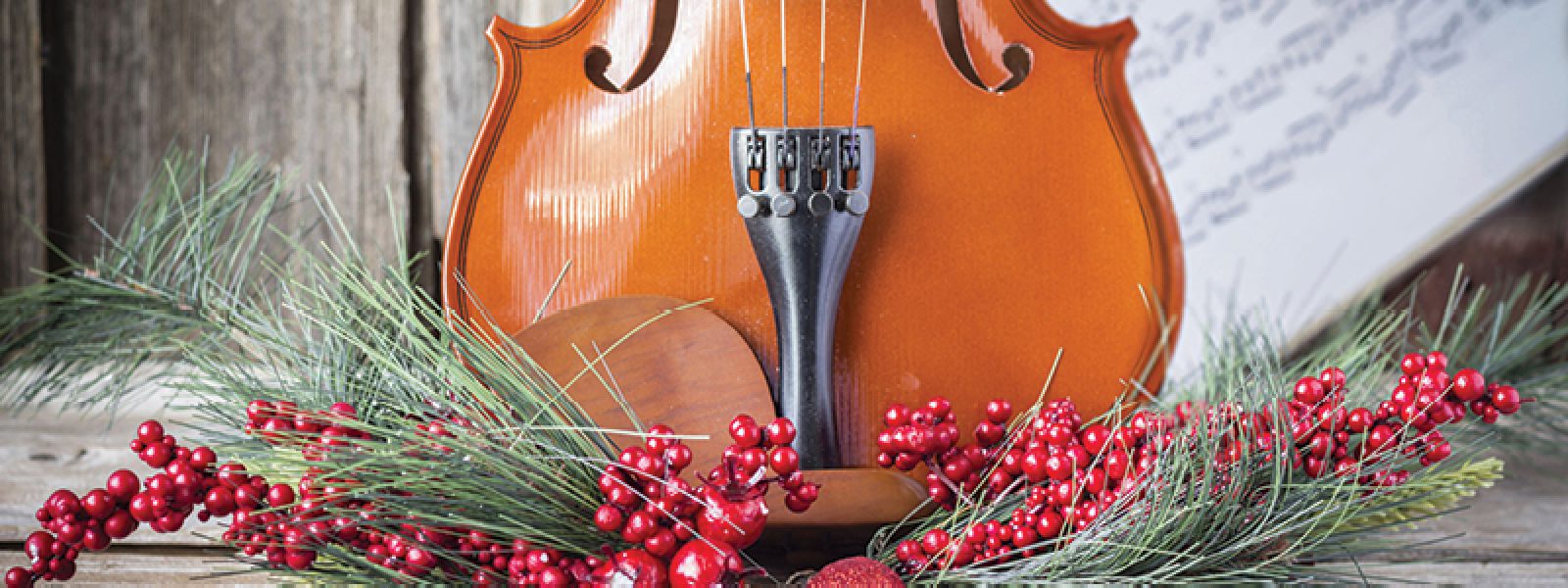 Violin in front of sheet music with pine, red berries, and red ornaments
