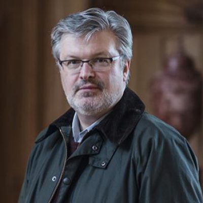 Person wearing glasses with a beard and short hair looks at the camera.