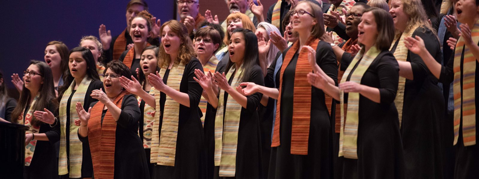 VocalEssence Singers wearing stoles and clapping their hands. Photo Credit: Bruce Silcox