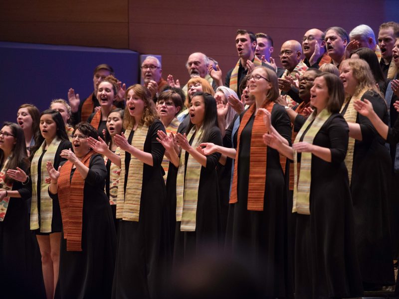 VocalEssence Singers wearing stoles and clapping their hands. Photo Credit: Bruce Silcox