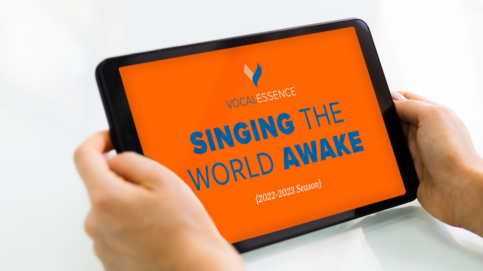 Hands holding tablet with VocalEssence logo, Singing the World Awake, and 2022-2023 Season on an orange background