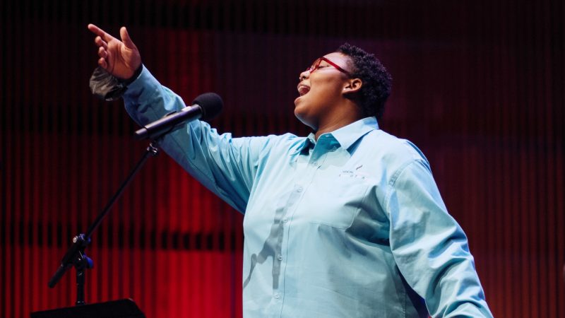 VocalEssence Singers Of This Age member sings into a microphone with hand outstretched