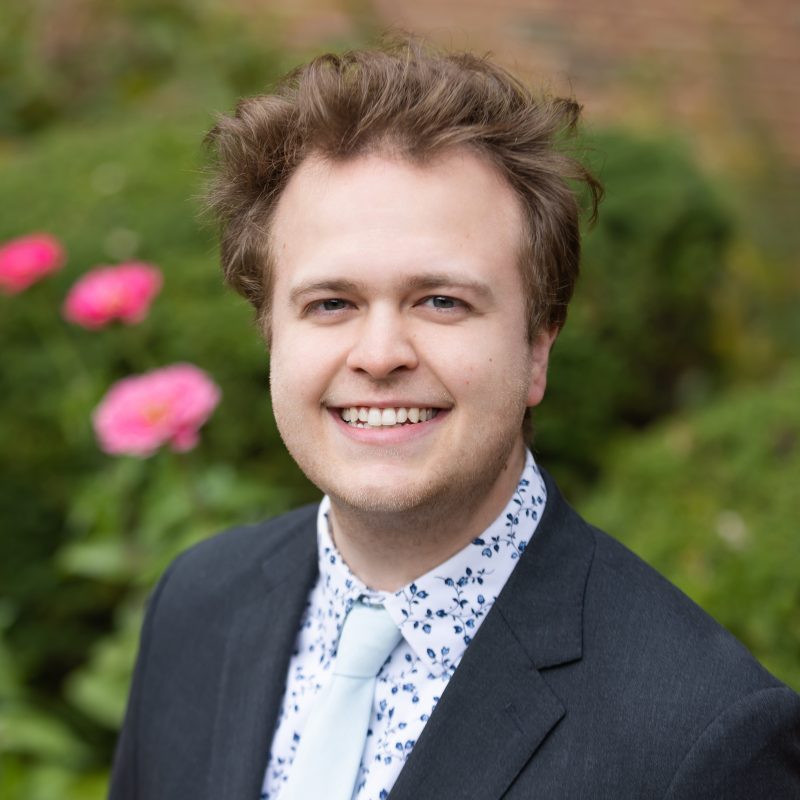 Foto de Ethan Johnson con traje y corbata sonriendo a la cámara.