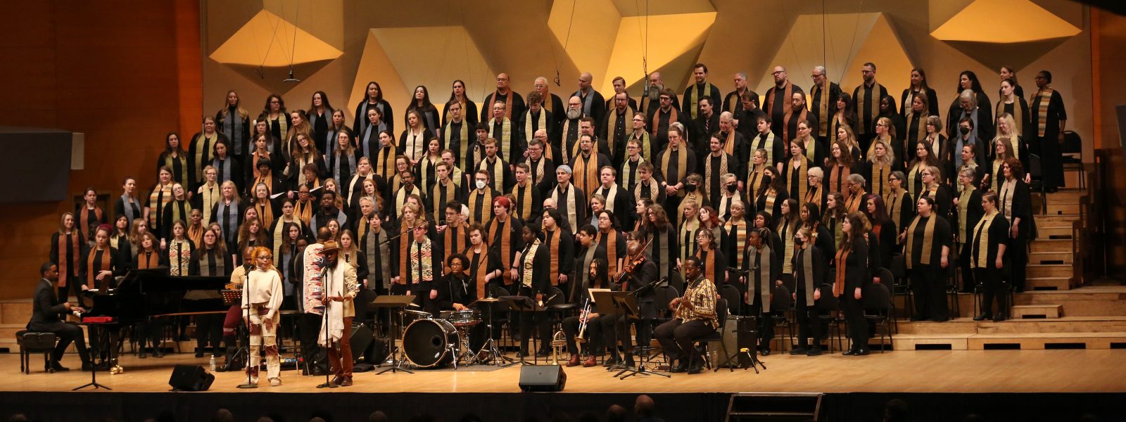 A large group of singers stands on the Orchestra Hall stage.