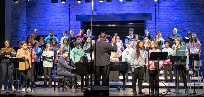 Singers performing on stage with a conductor.