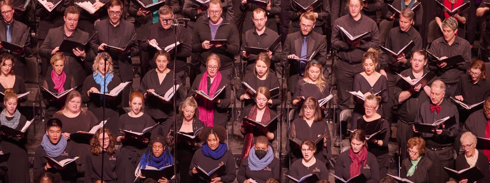Singers wearing black clothes and multicolored scarves holding black folders perform