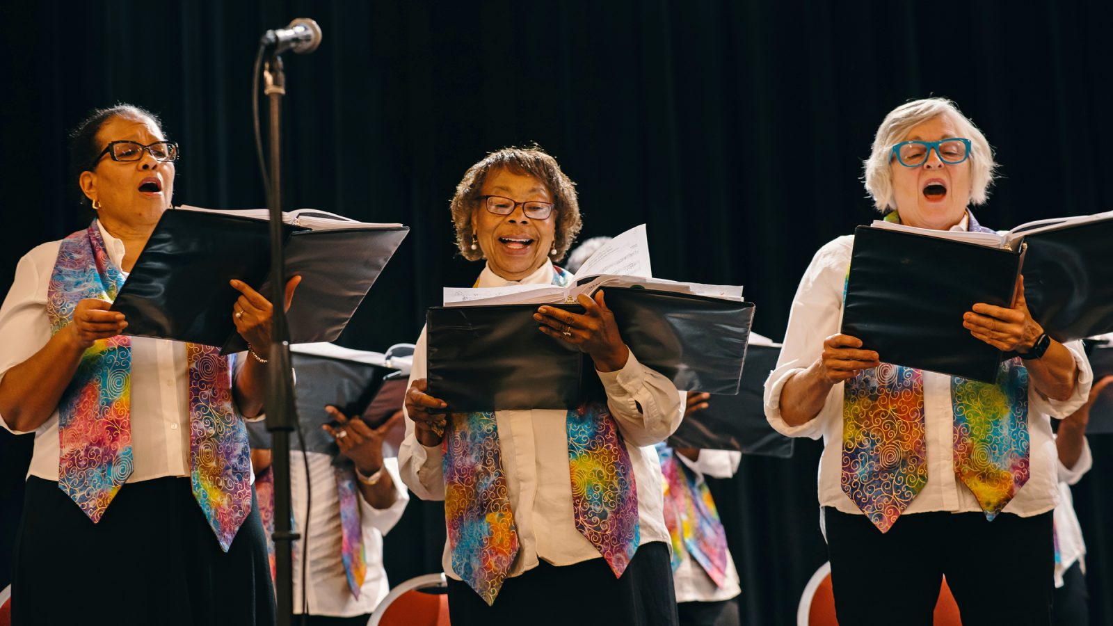 Tres miembros adultos de Vintage Voices sosteniendo carpetas negras y cantando. Crédito de la foto: Adja Gildersleve