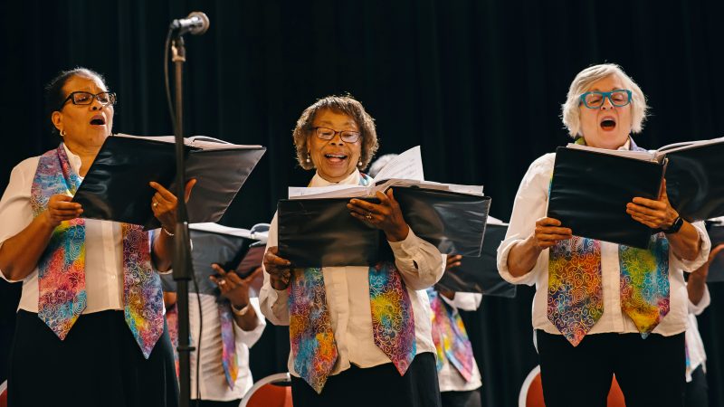 Three adult Vintage Voices members holding black folders and singing. Photo Credit: Adja Gildersleve