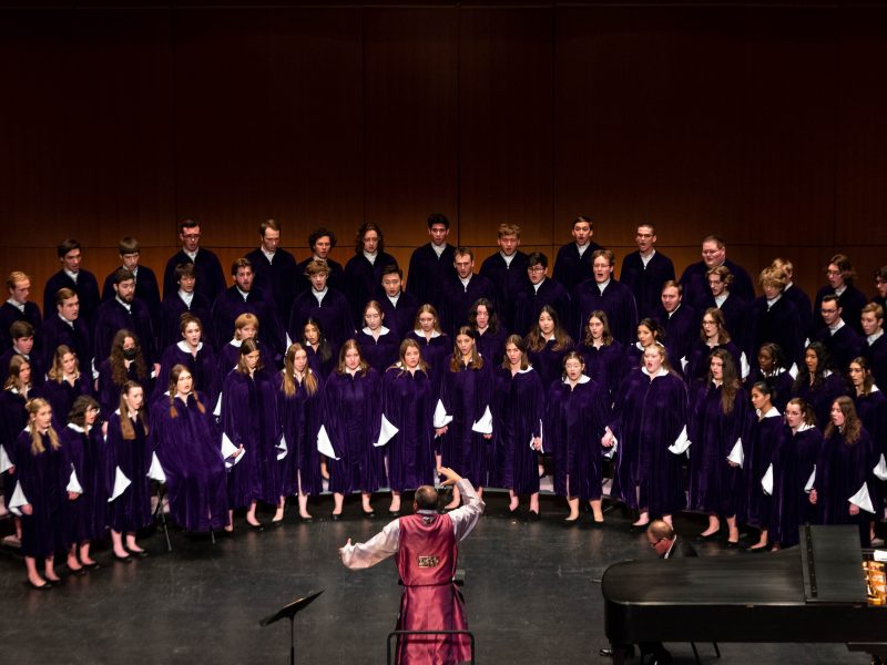 Conductor wearing a red robe in front of singers in blue robes