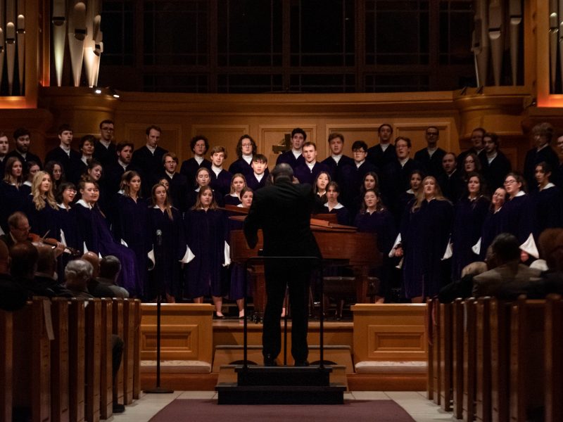 Conductor wearing black suit in front of singers in blue robes