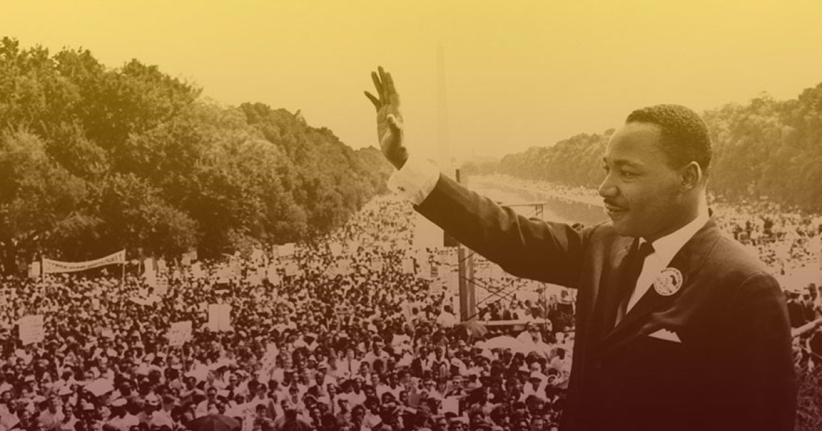 Dr. Martin Luther King, Jr. raises a hand in front of crowds of people at the Lincoln Memorial.