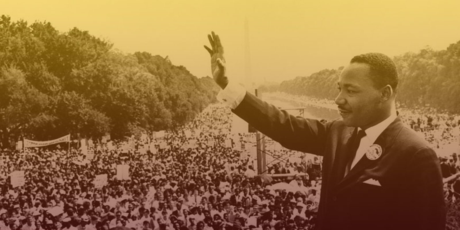 Dr. Martin Luther King, Jr. raises a hand in front of crowds of people at the Lincoln Memorial.