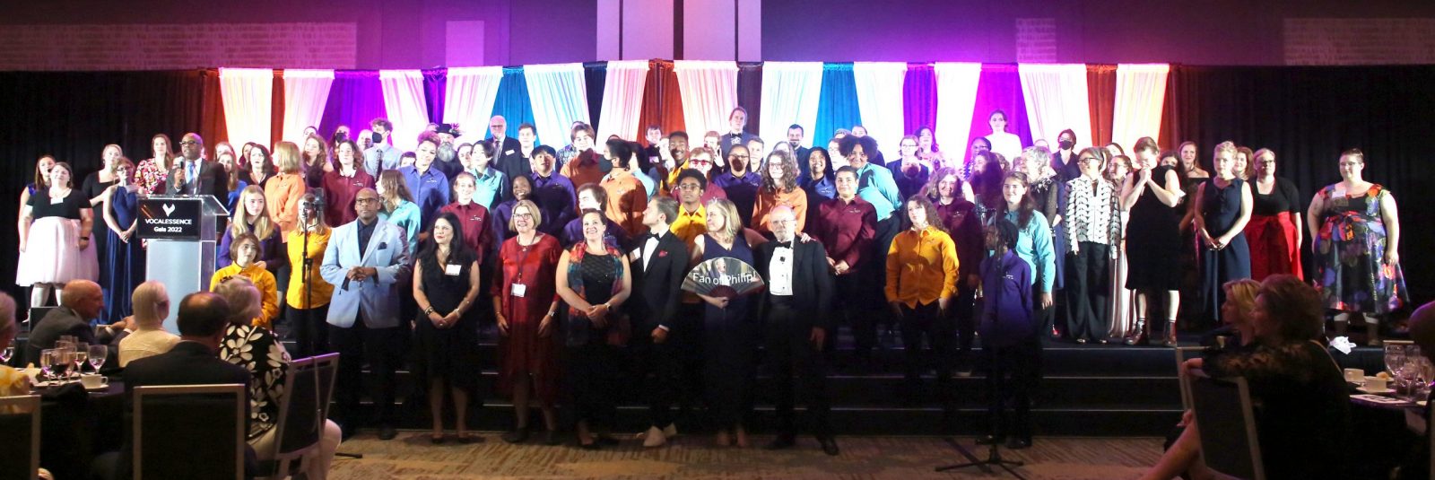9Q5A1330 VocalEssence singers and staff stand on stage applauding the conclusion of a gala.