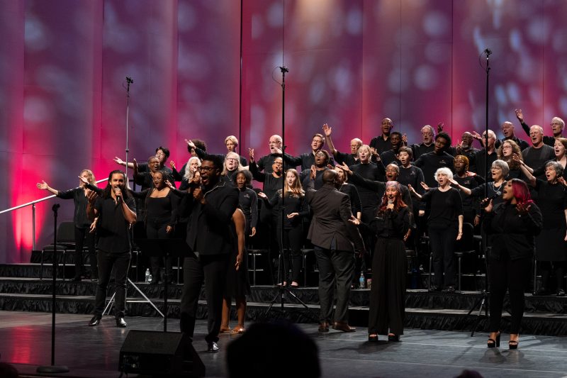 Singers performing on stage with their hands raised.