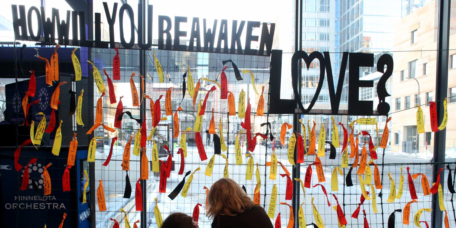 People in front of display with different colored ribbons and the question, How Will You Reawaken Love? Photo credit: Kyndell Harkness