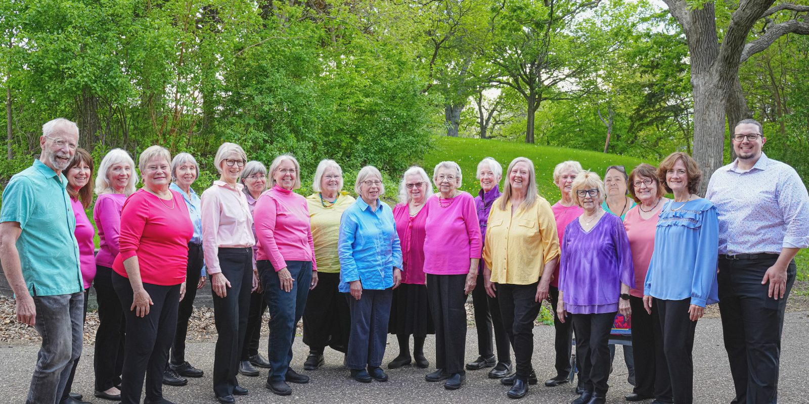 Keystone Fall 2024 Event Page 2400x1200 Adult Vintage Voices members wearing colorful shirts and black pants standing in a row and smiling standing in front of bright green trees and grass. Photo Credit: Novelli Jurado, Novart Media