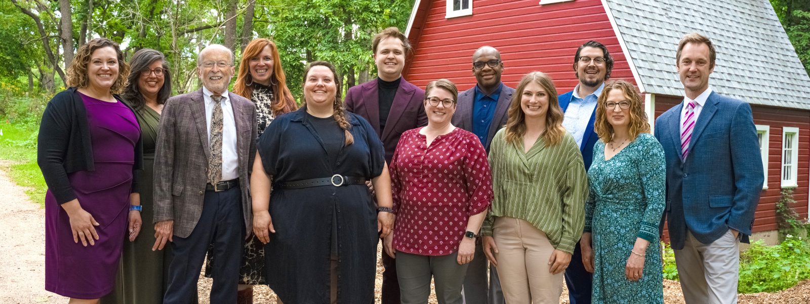 Members of the VocalEssence staff pose for a photo in front of a red barn surrounded by greenery. Photo credit: Novelli Jurado, Novart Media