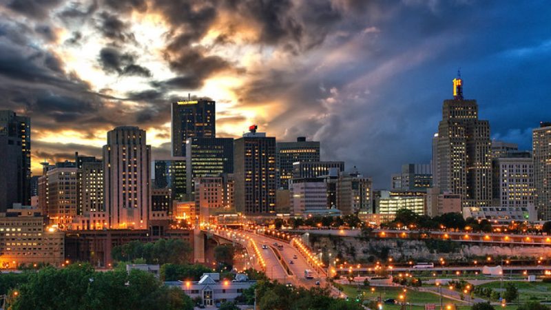 The skyline of downtown Saint Paul, Minnesota with a sky of dark storm clouds and hints of the sun breaking through. Photo Credit: Dan Anderson.