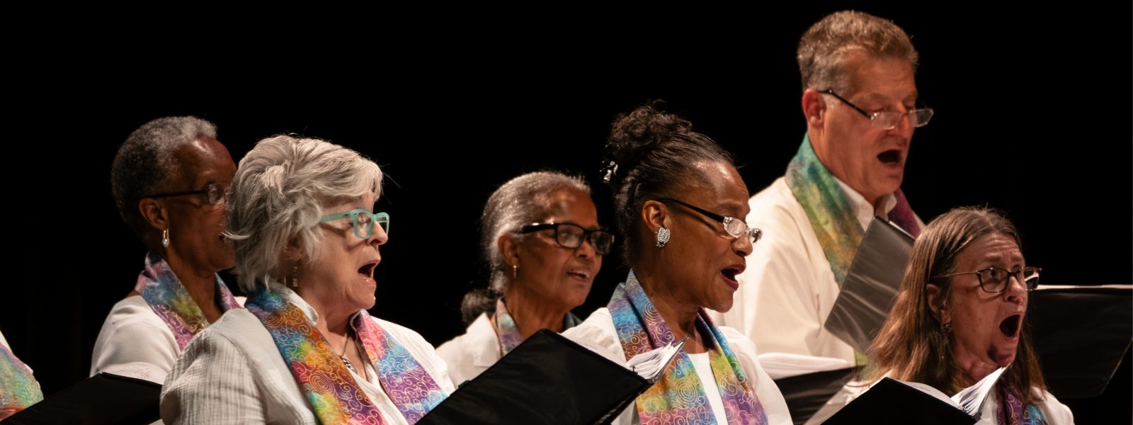 Vintage Voices Singers performing wearing white shirts and multi-colored pastel stoles. Photo credit: Ethan Kellum Johnson.