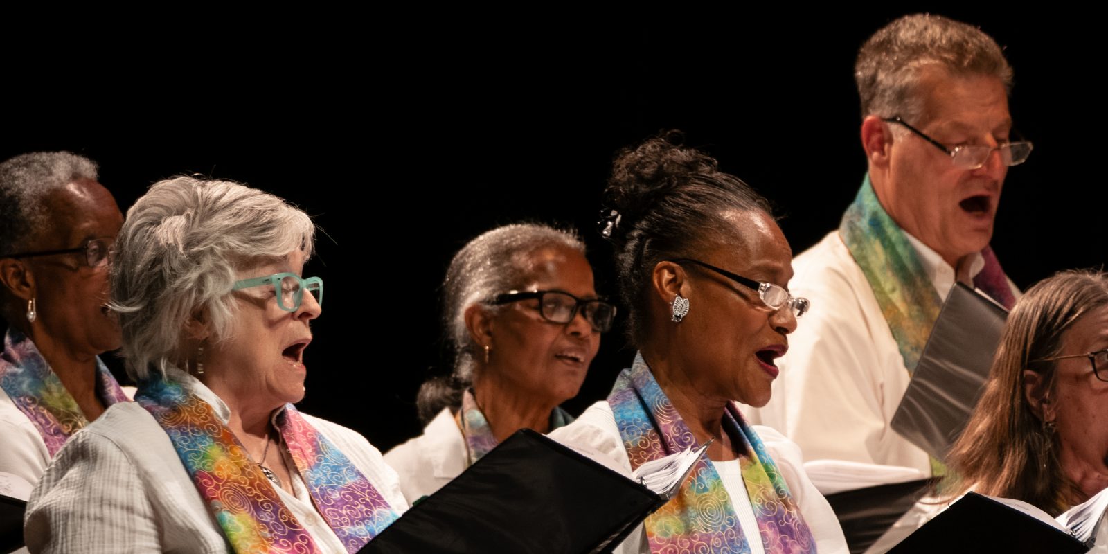 Vintage Voices Singers performing wearing white shirts and multi-colored pastel stoles. Photo credit: Ethan Kellum Johnson.