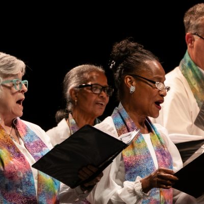 Vintage Voices Singers performing wearing white shirts and multi-colored pastel stoles. Photo credit: Ethan Kellum Johnson.