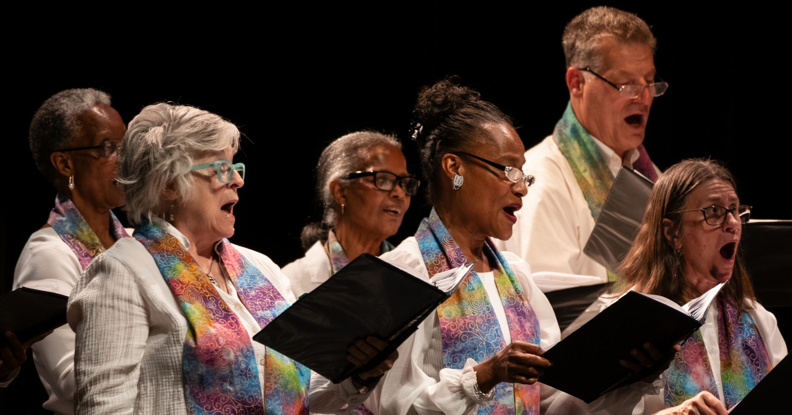 Vintage Voices Singers performing wearing white shirts and multi-colored pastel stoles. Photo credit: Ethan Kellum Johnson.