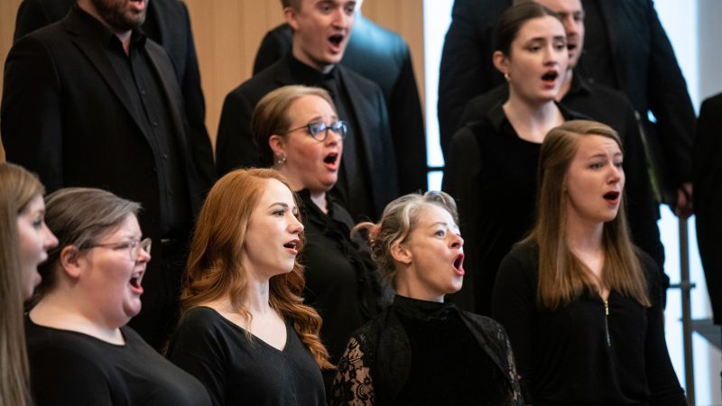VocalEssence Ensemble Singers wearing black perform with joyful expressions. Photo Credit: Bruce Silcox