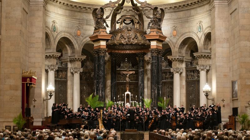 Many singers perform in front of an audience in the ornate sanctuary of the Cathedral of Saint Paul that features a baldachin with black and gold marble columns that has a bronze latticework canopy. Photo Credit: Bruce Silcox