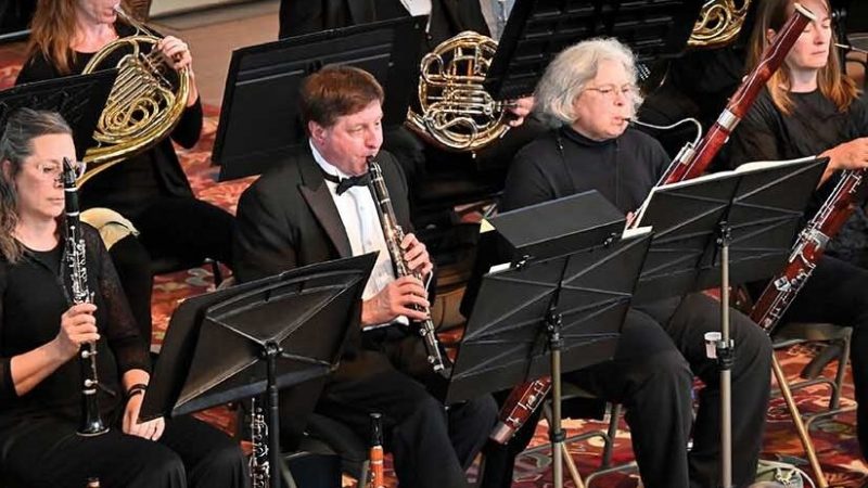 Members of the Metropolitan Symphony Orchestra wearing black, sitting, playing their instruments, with black music stands.