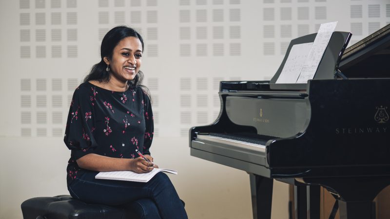 Shruthi Rajasekar wearing a black floral top sits holding a pencil and a notebook. Photo Credit: Roscoe Rutter