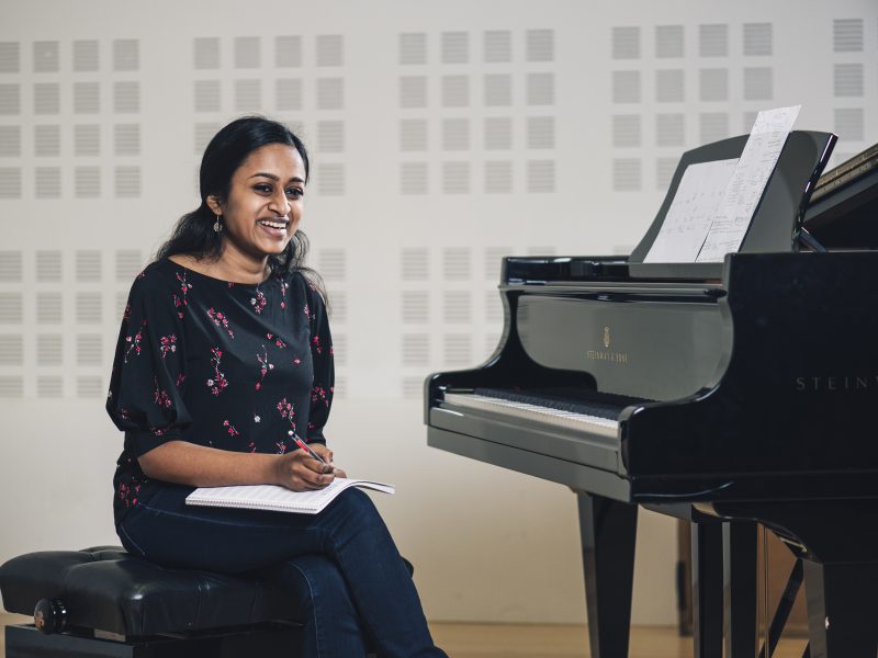 Shruthi Rajasekar wearing a black floral top sits holding a pencil and a notebook. Photo Credit: Roscoe Rutter