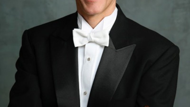 Person in black tuxedo holding a baton..