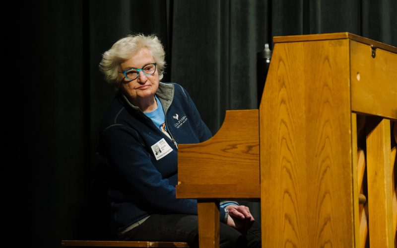 Woman with glasses and short hair wearing a blue top looks around a piano. Photo credit: Laura Alpizar