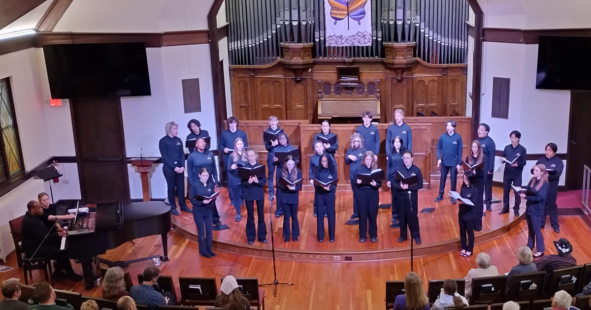 VocalEssence Singers Of This Age, wearing blue shirts and black pants holding black folders sing in the sanctuary of a church. Photo credit: Rhiannon Fiskradatz