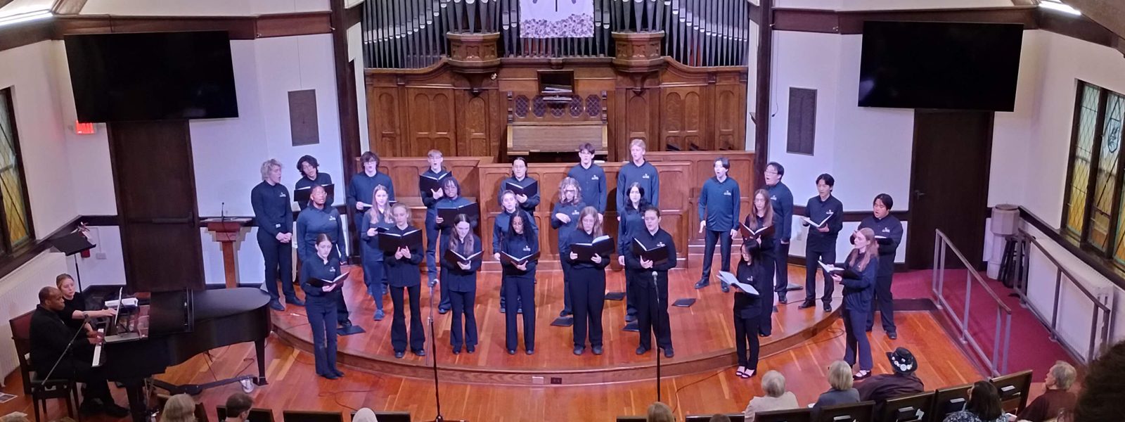VocalEssence Singers Of This Age, wearing blue shirts and black pants holding black folders sing in the sanctuary of a church. Photo credit: Rhiannon Fiskradatz