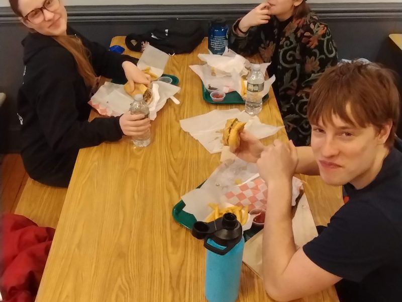 People sitting at a table eating Philly cheesesteaks.