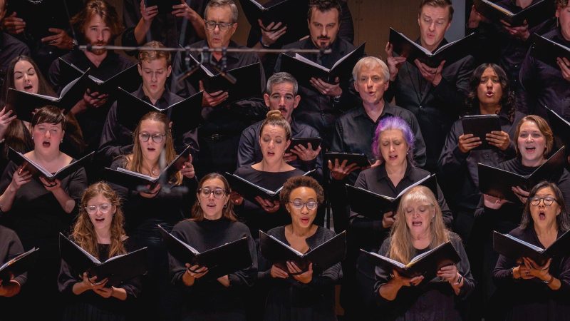 Members of the VocalEssence Chorus wearing black, holding black folders, and singing. Photo Credit: Novart Media