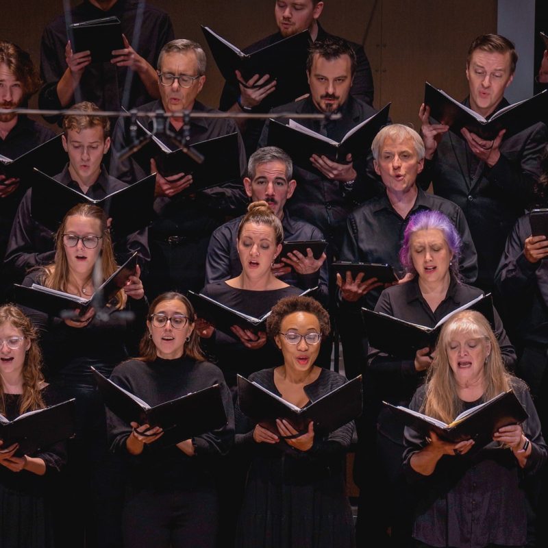 Members of the VocalEssence Chorus wearing black, holding black folders, and singing. Photo Credit: Novart Media