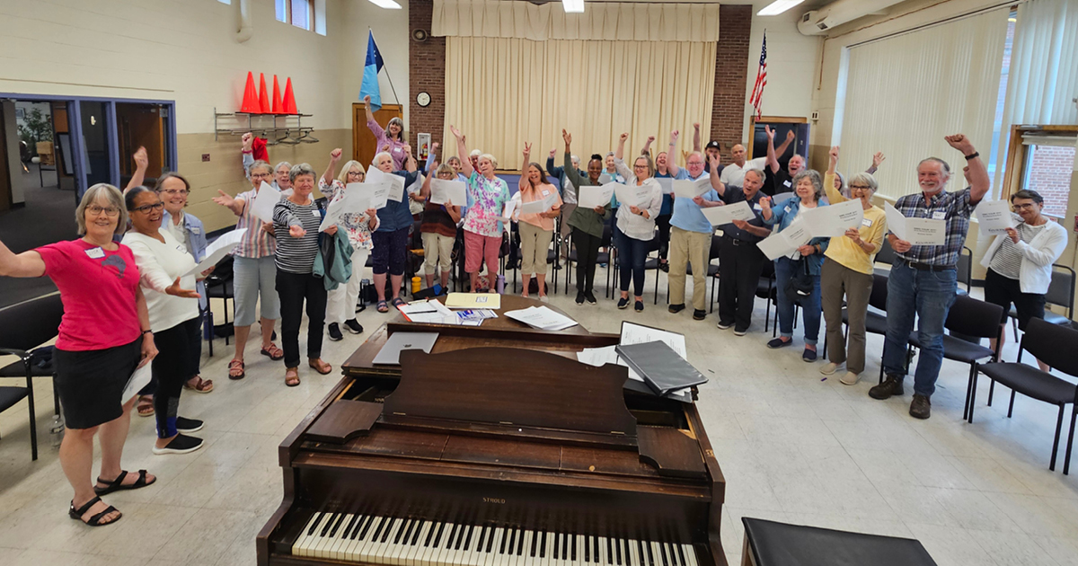 Image of singers with their hands up around a piano. Photo Credit: Robert Graham