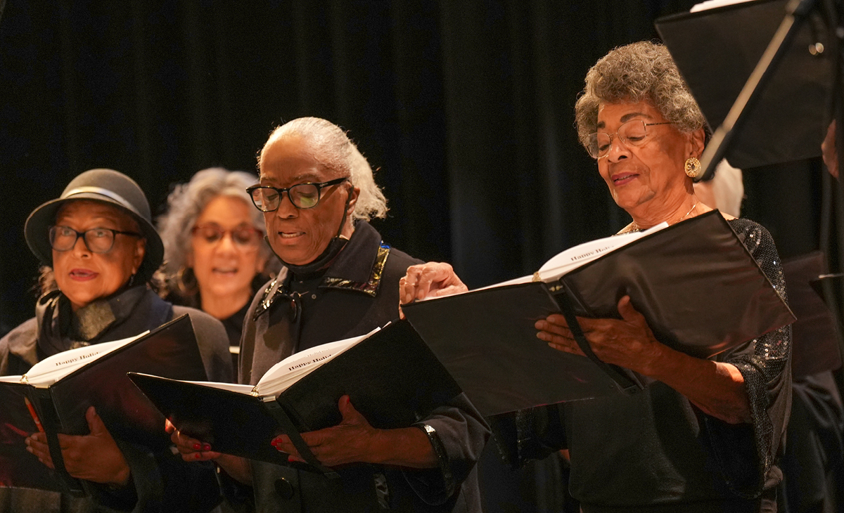 Adult Vintage Voices members wearing all black holding black folders and singing in front of a black curtain. Photo Credit: Novart Media.