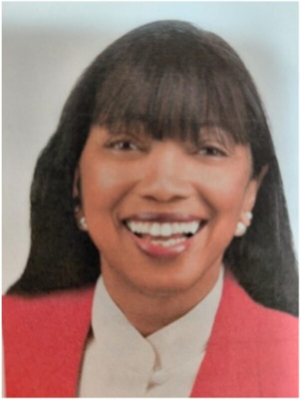 Person with long black hair and earrings wearing a white shirt with a coral colored blazer.