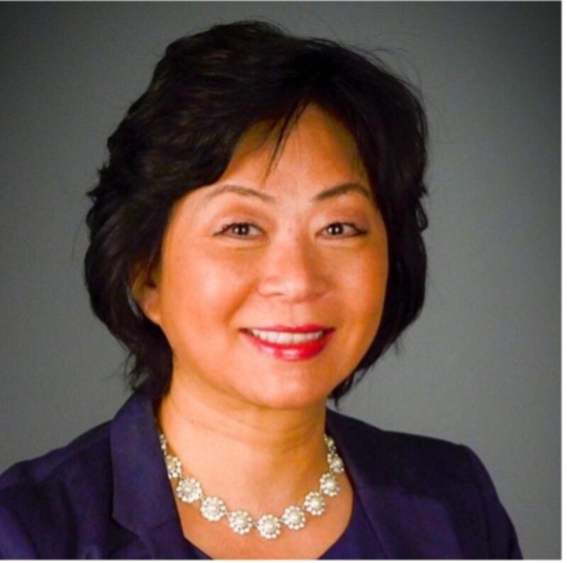 Image of person with short dark hair wearing a dark colored blazer and silver circle necklace.